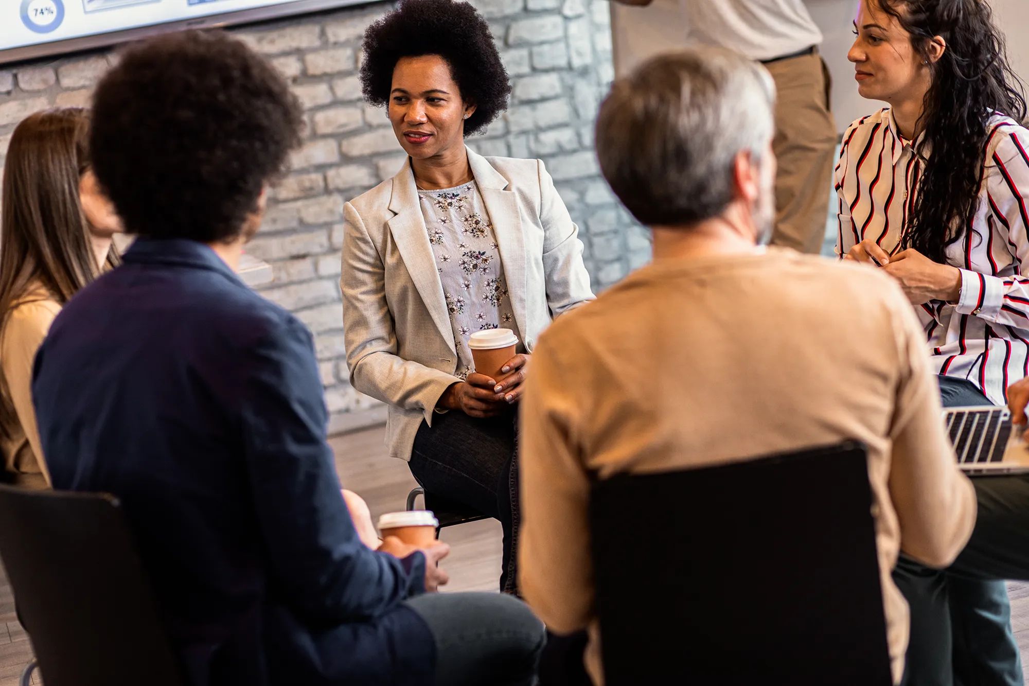 A group of professionals seated in a circle talking holding coffee cups.