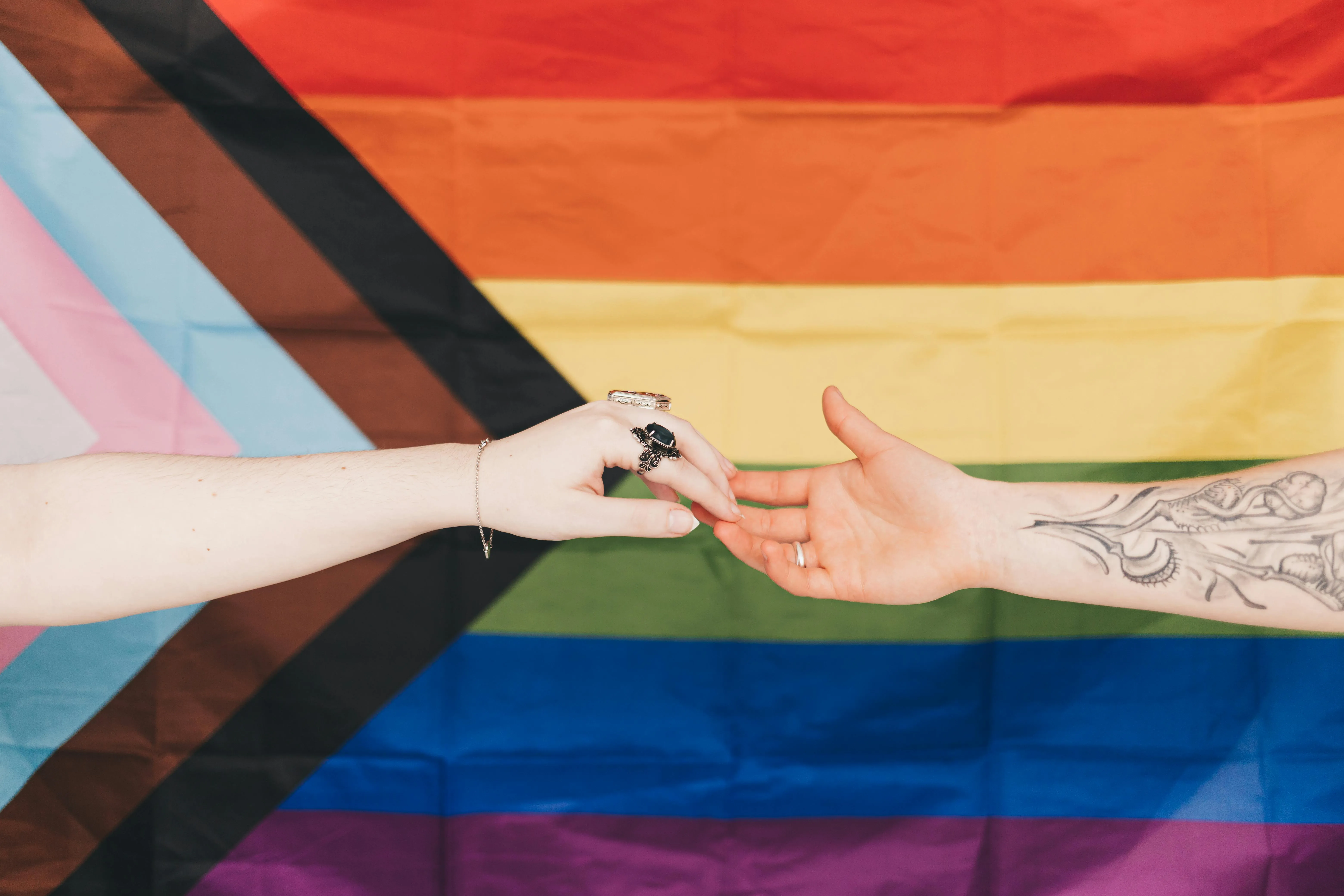 Two outreached hands grazing finger tips in front of a pride flag.