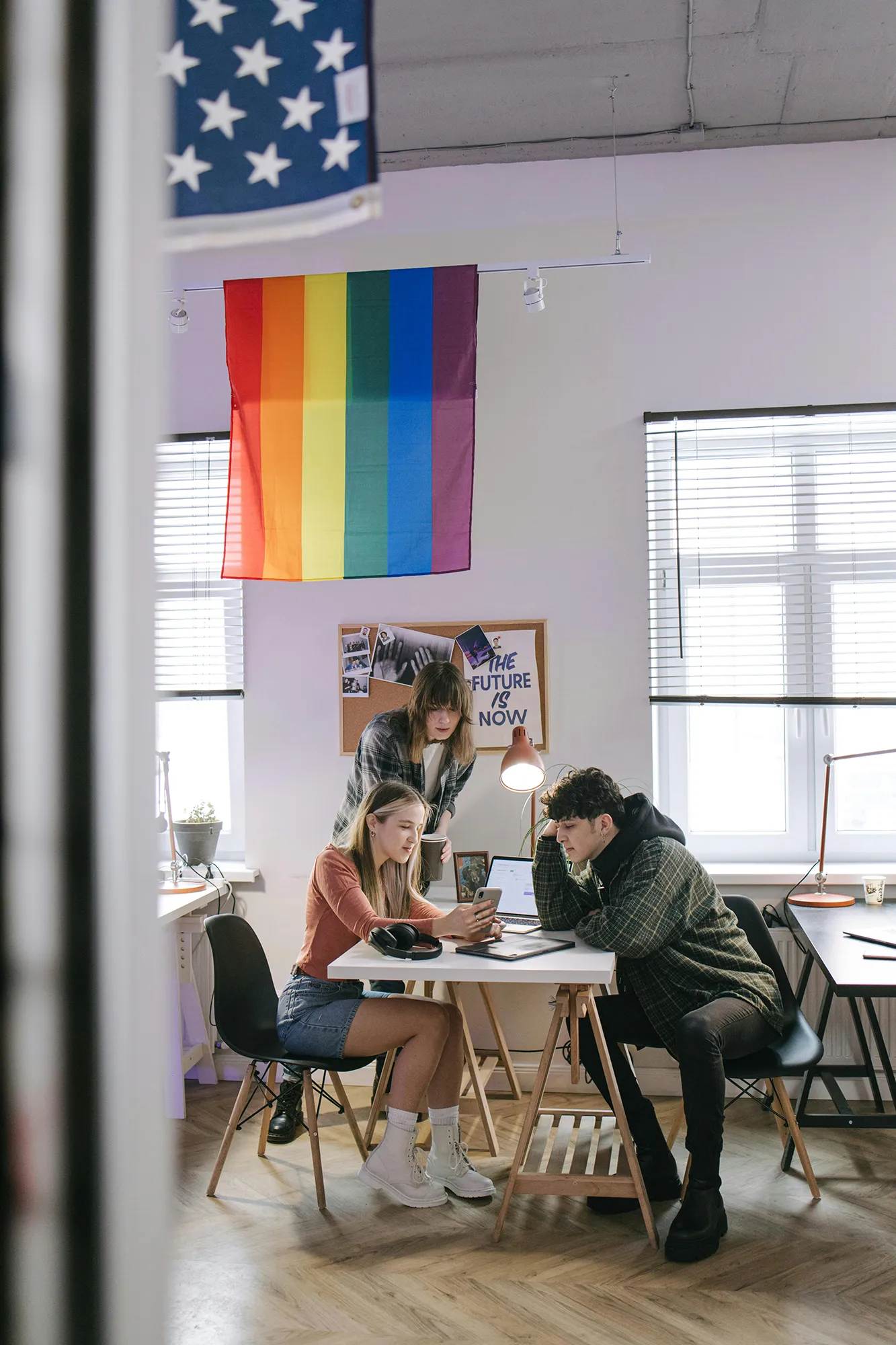 Office meeting with three people in front of a rainbow working at a desk.