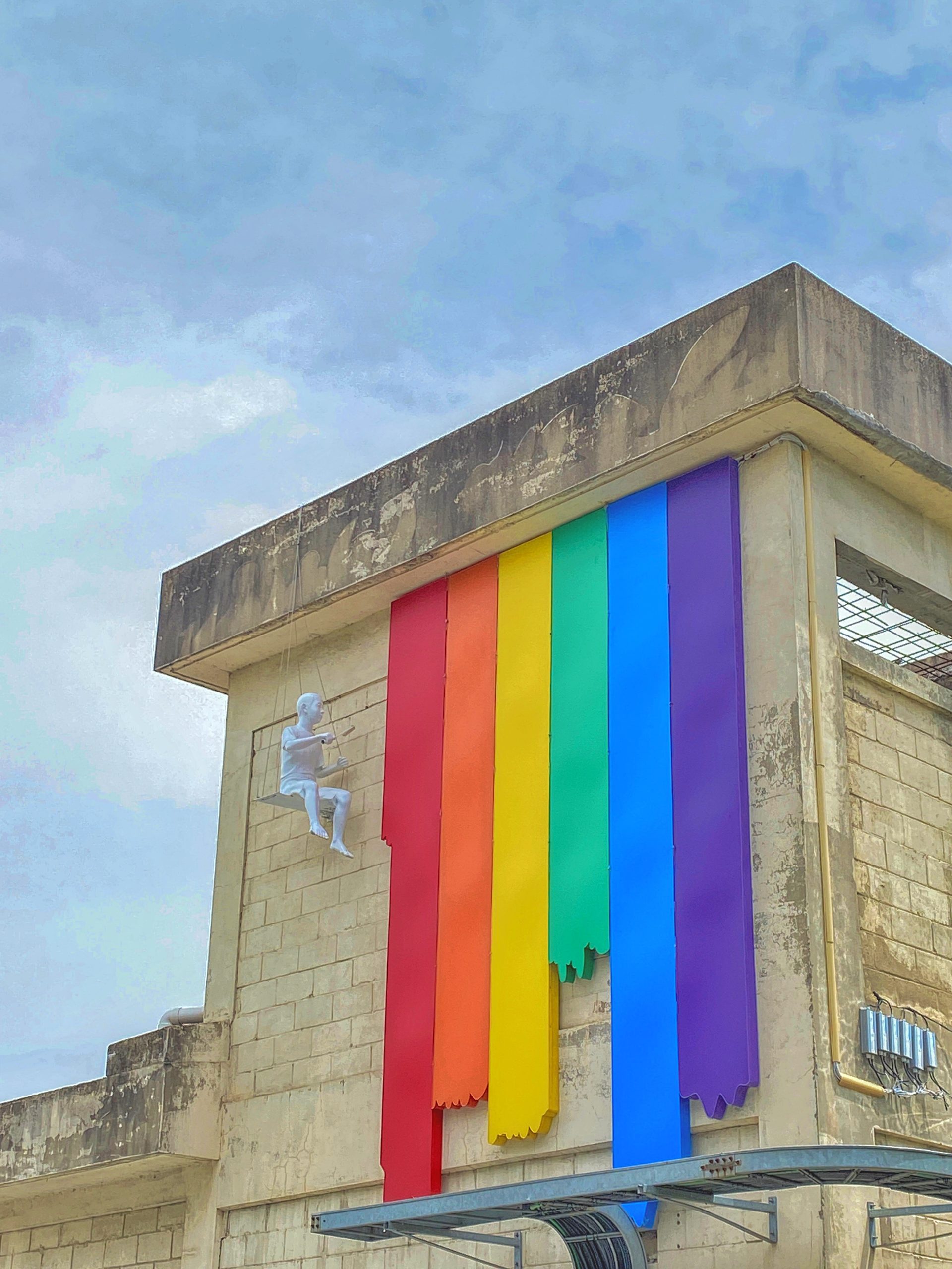 Sandstone building with rainbow stripes and a sculpture of a person scaling the building