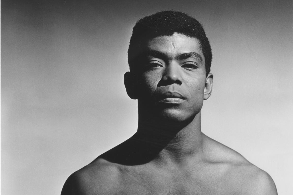 Black and white portrait of Alvin Ailey, a Black man with cropped natural hair, staring at the camera. 