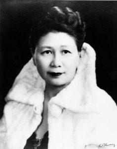 A black and white photograph of Dr. Margaret Chung, a Chinese American woman wearing a white fut coat, stylish updo, and dark lipstick.