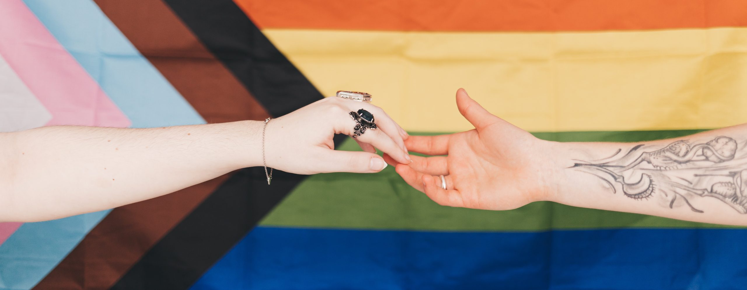 Two outreached hands grazing finger tips in front of a pride flag.