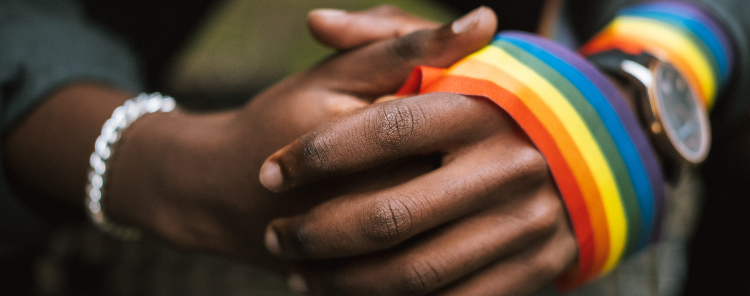 Two clasped hands wrapped in a rainbow ribbon