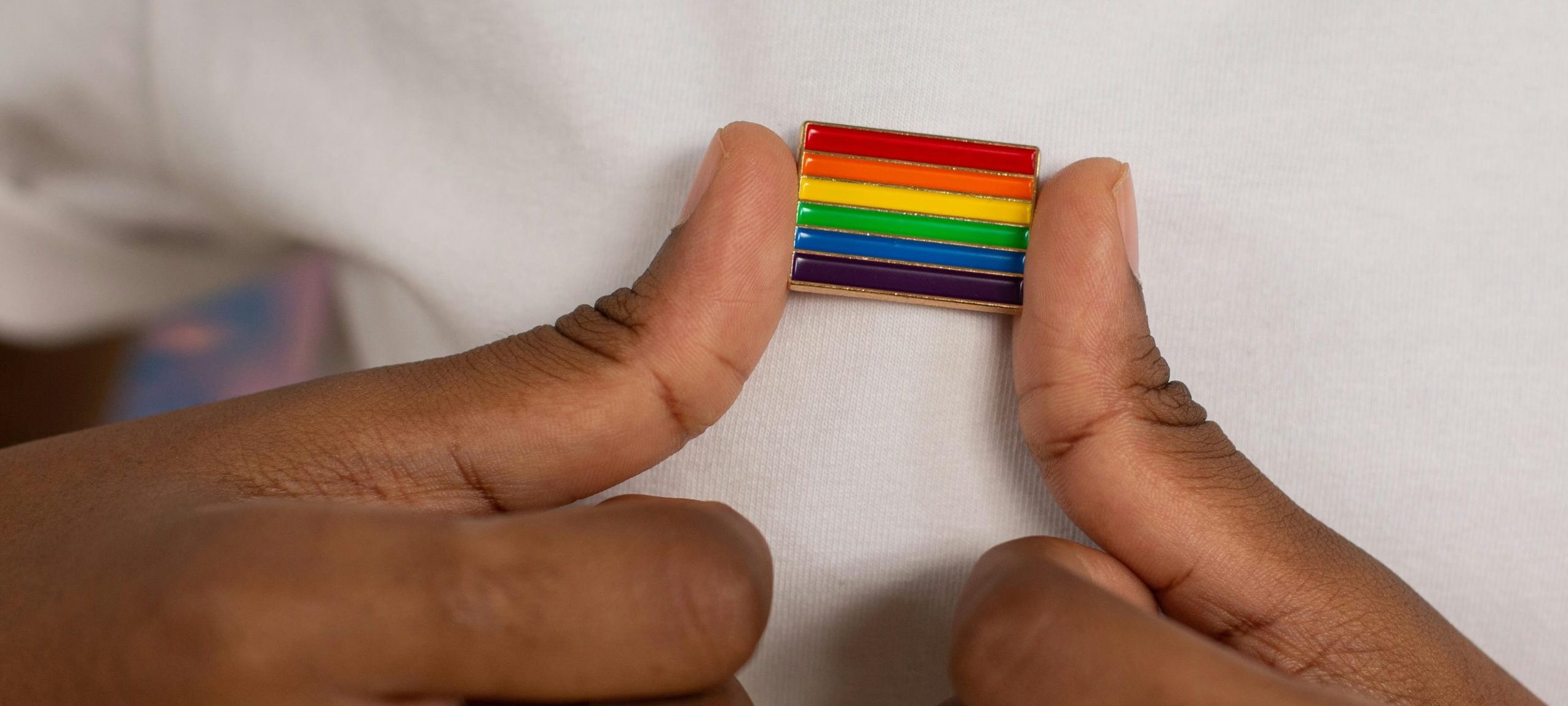 Close up of hands, medium-dark skin tone, holding a rainbow pin.