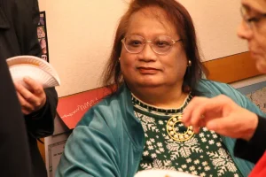 A color photograph of Tamara Ching, a middle-aged, transgender, Chinese  woman, who is seated at a meeting.